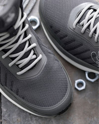 Close-up of a pair of dark gray athletic sneakers with white laces, shown on a textured gray stone surface with small metal hexagonal nuts as props.