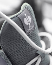 Close-up of a gray mesh sneaker with white laces, showing a gray tongue label with the white Strauss logo and brand name.