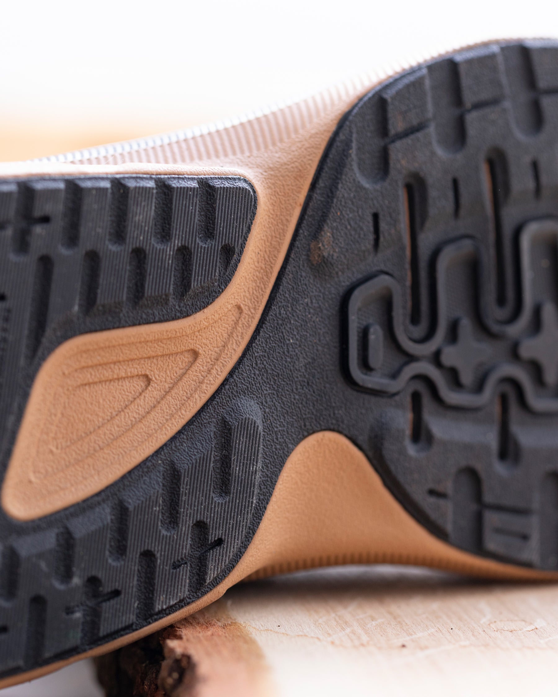 Close-up of the outsole of a sneaker, showing a black treaded rubber bottom with a tan and beige midsole section.