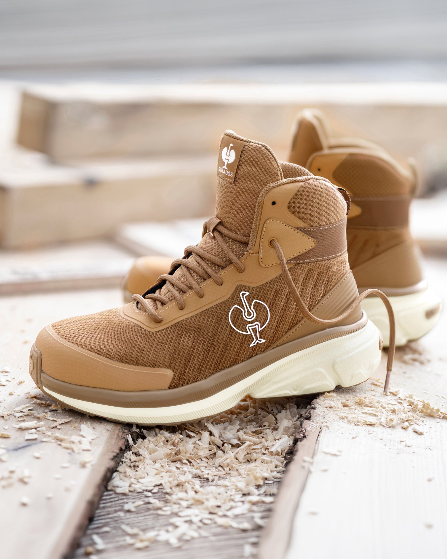A pair of tan and brown high-top athletic sneakers with a white sole, featuring a white rooster logo on the side and tongue, displayed on weathered wooden planks outdoors.