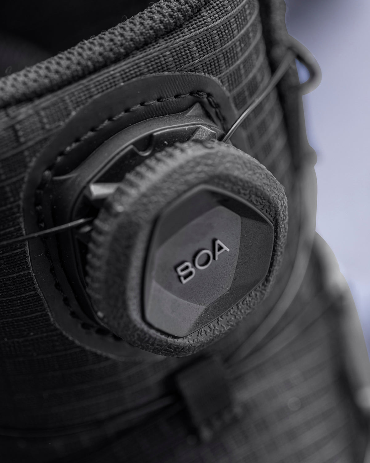 Close-up of a black BOA dial closure system on a textured black boot, showing the brand name 'BOA' on the hexagonal dial.