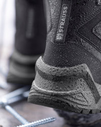 Close-up of a black Draupus Strauss waterproof boot with water droplets on the textured rubber sole and upper, showing the brand label on the heel.