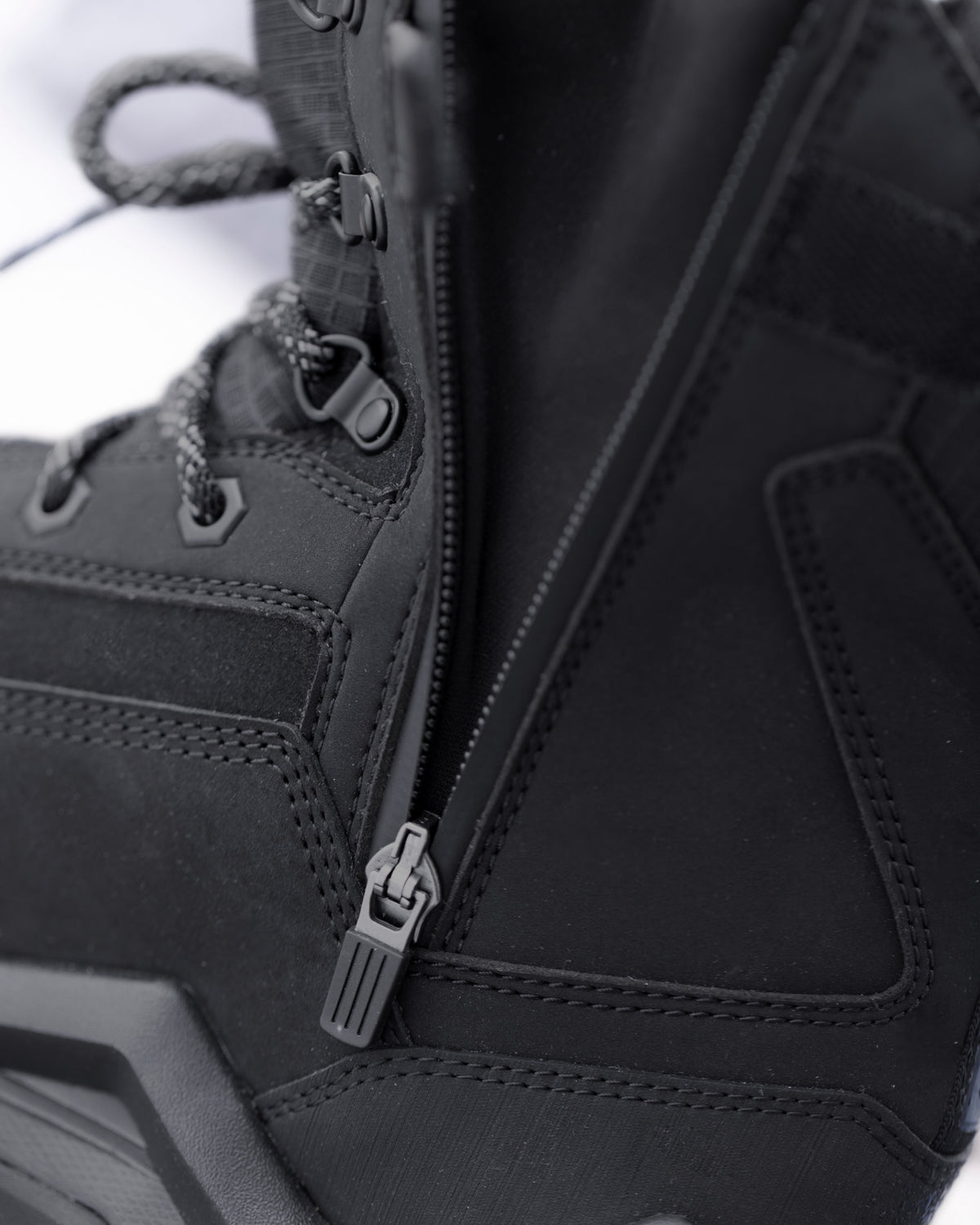 Close-up detail of a black high-top boot showing the side zipper, laces, stitching, and zipper pull hardware.
