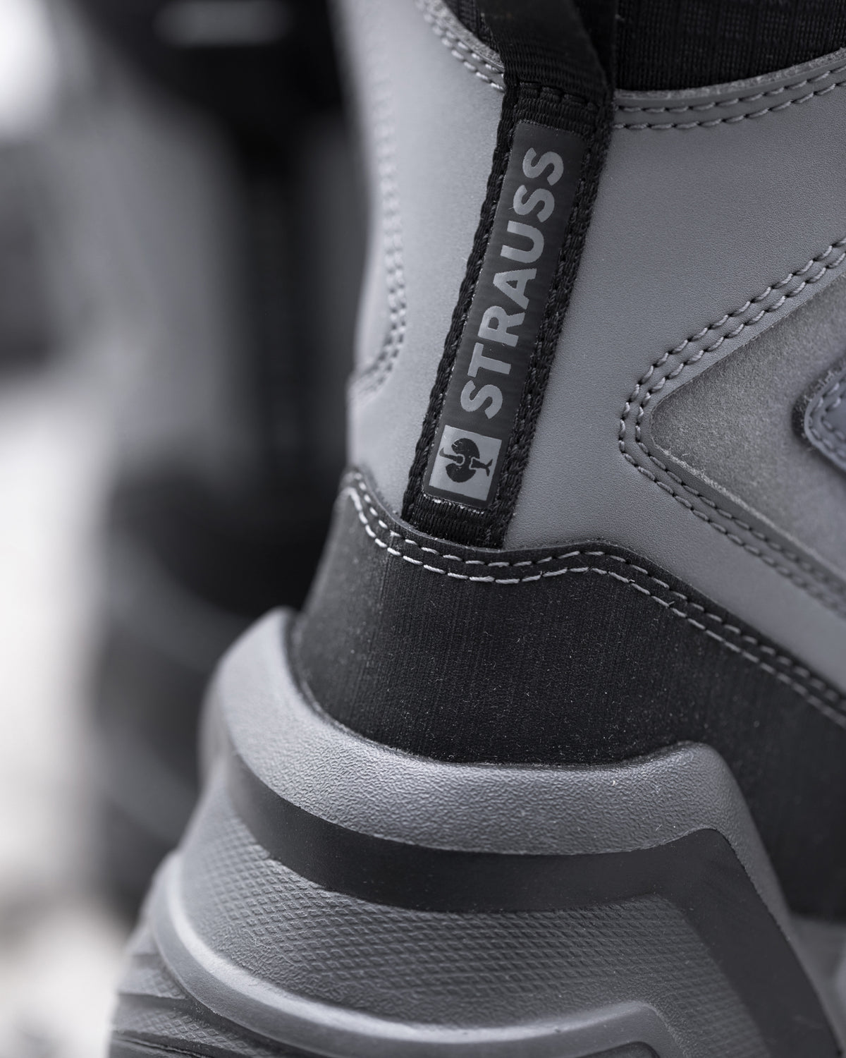 Close-up of a gray and black boot with a black pull tab displaying the brand name 'STRAUSS'.
