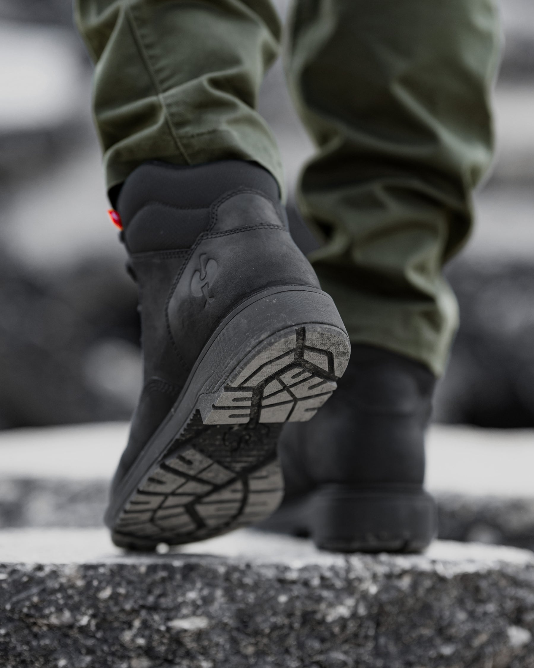 A close-up shot of a person's feet wearing black high-top boots and olive green pants, walking on a wet, dark asphalt surface.