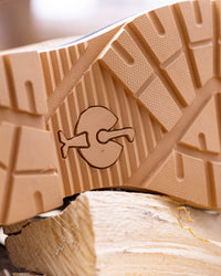 Close-up of a tan rubber shoe sole with a carved logo, resting on a piece of light wood.