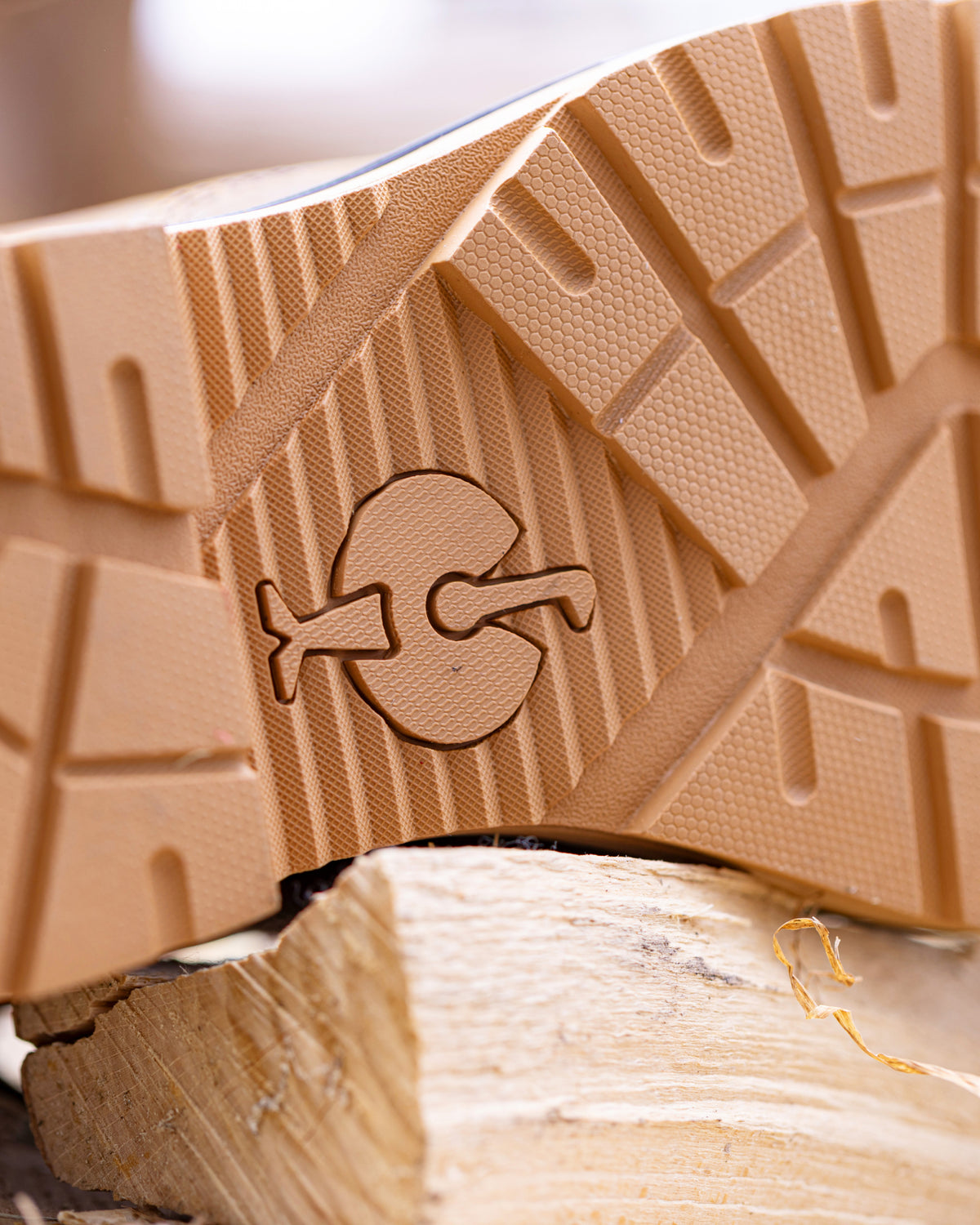 Close-up of a tan rubber shoe sole with a carved logo, resting on a piece of light wood.