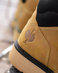 Close-up of a tan suede high-top shoe with a black sock inserted, showing a debossed logo on the heel and a thick tan sole.