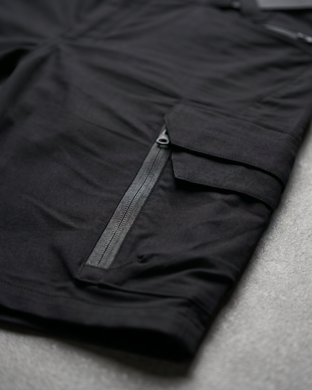 Close-up detail of Engelbert Strauss e.s. trail pure cargo work shorts in black and carbon gray, focusing on the utility pocket area, seams, and reinforced workwear construction.