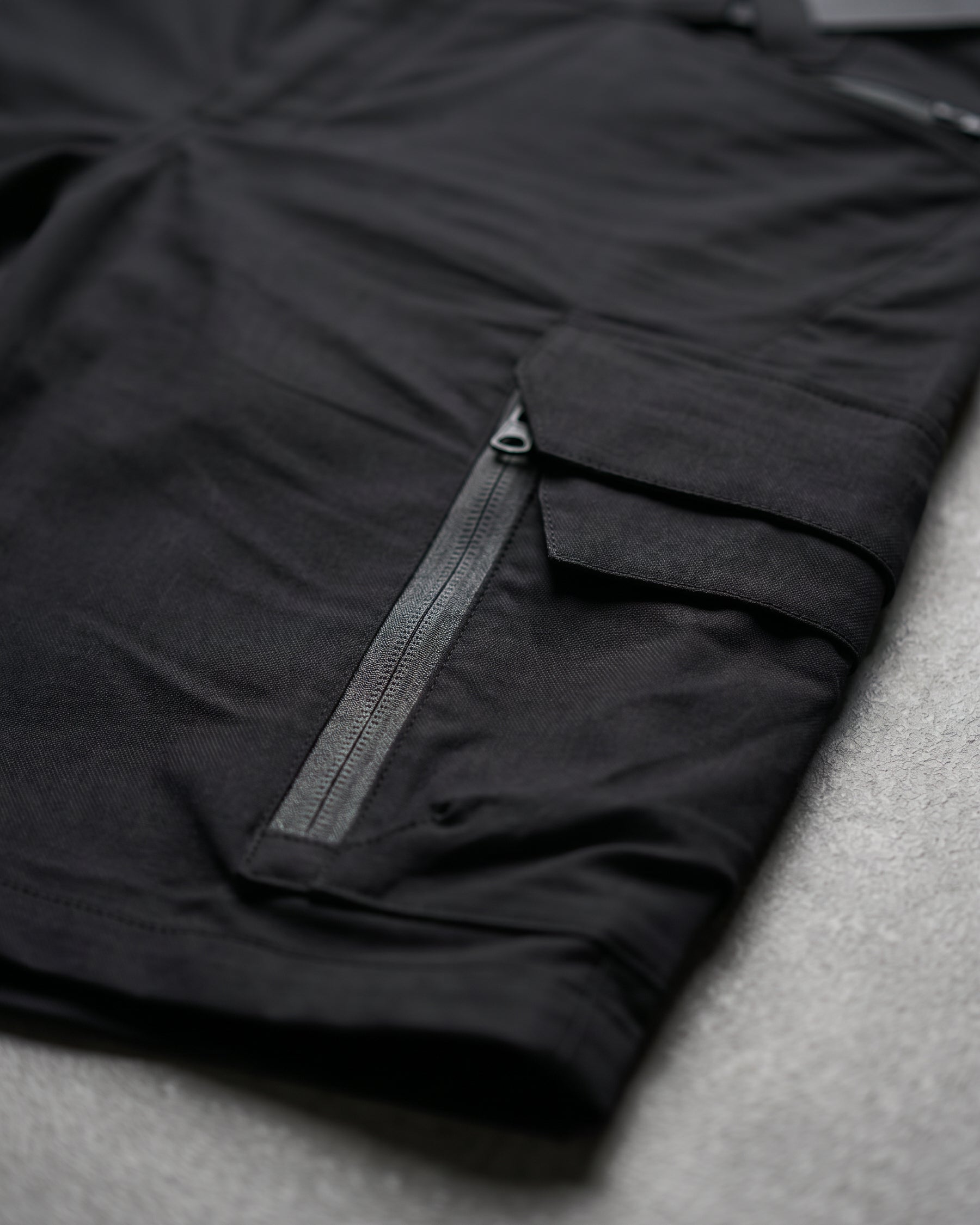 Close-up detail of Engelbert Strauss e.s. trail pure cargo work shorts in black and carbon gray, focusing on the utility pocket area, seams, and reinforced workwear construction.