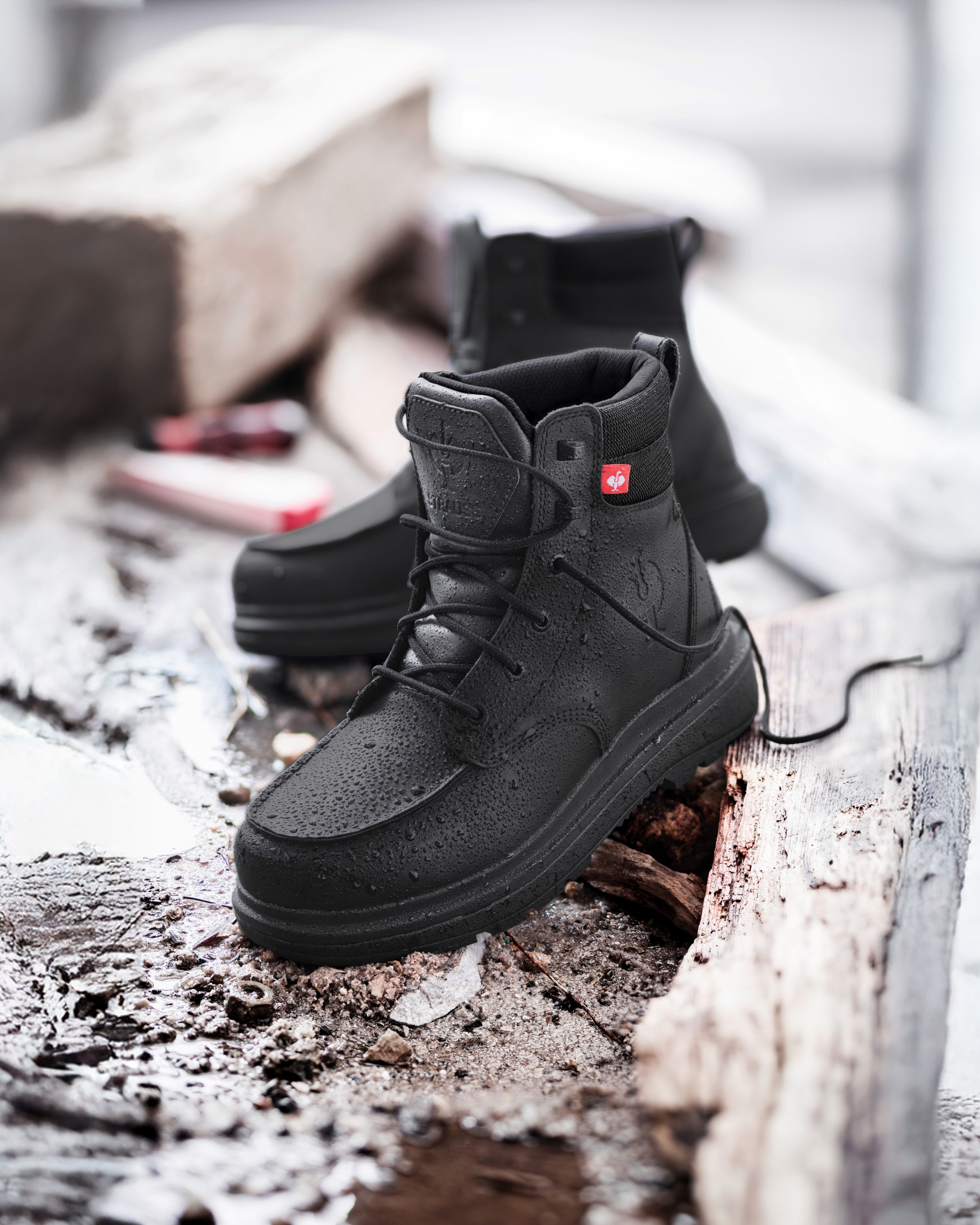 Black boots with rain drops and a red label on a rustic wooden surface