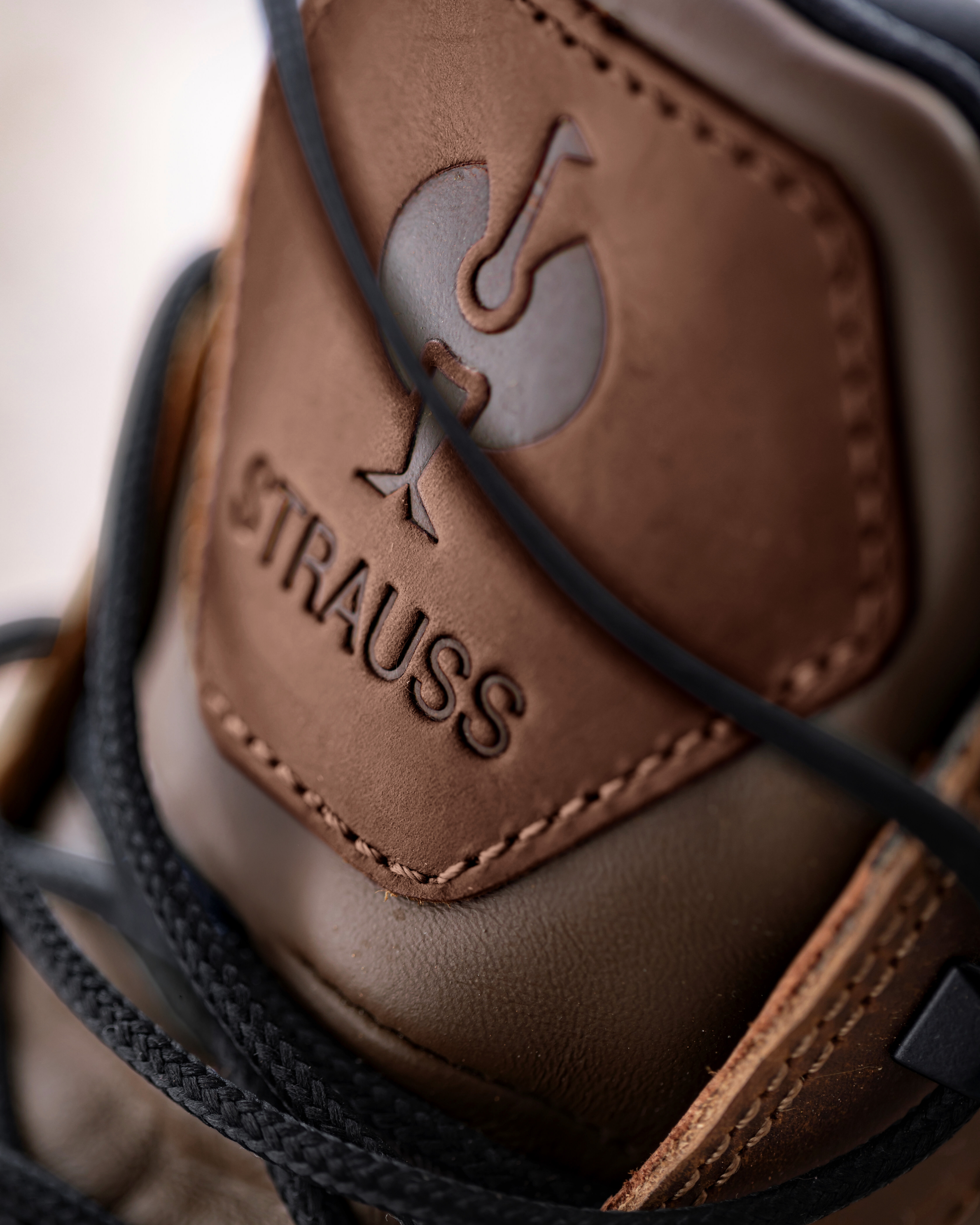Close-up of the tongue of a brown work boot with 'Strauss' branding on a blurred background