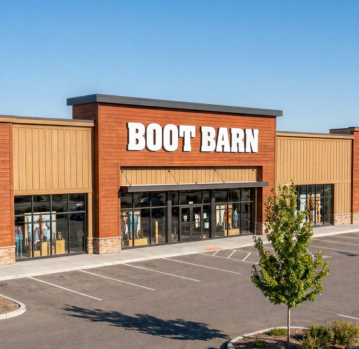 An image of a Boot Barn store. In front of the store there is a parking lot with trees.