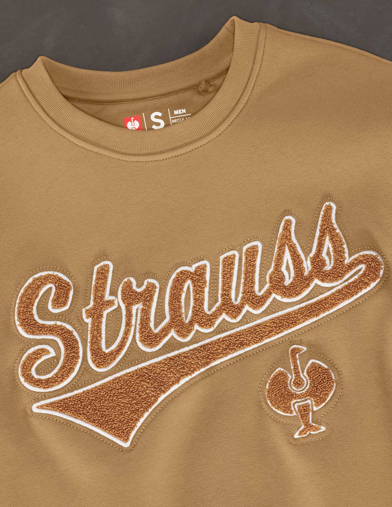 Brown sweatshirt with 'Strauss' branding on a dark background