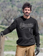 Man wearing a black 'Strauss' sweatshirt outdoors with greenery in the background