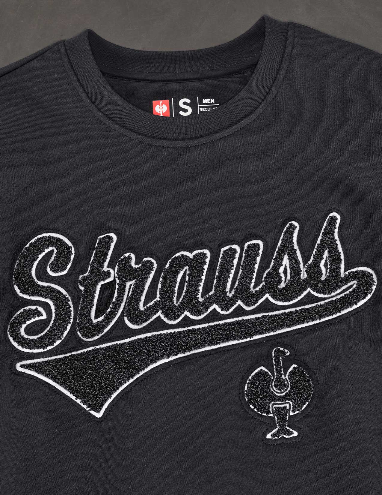 Black sweatshirt with 'Strauss' branding and logo on a dark background