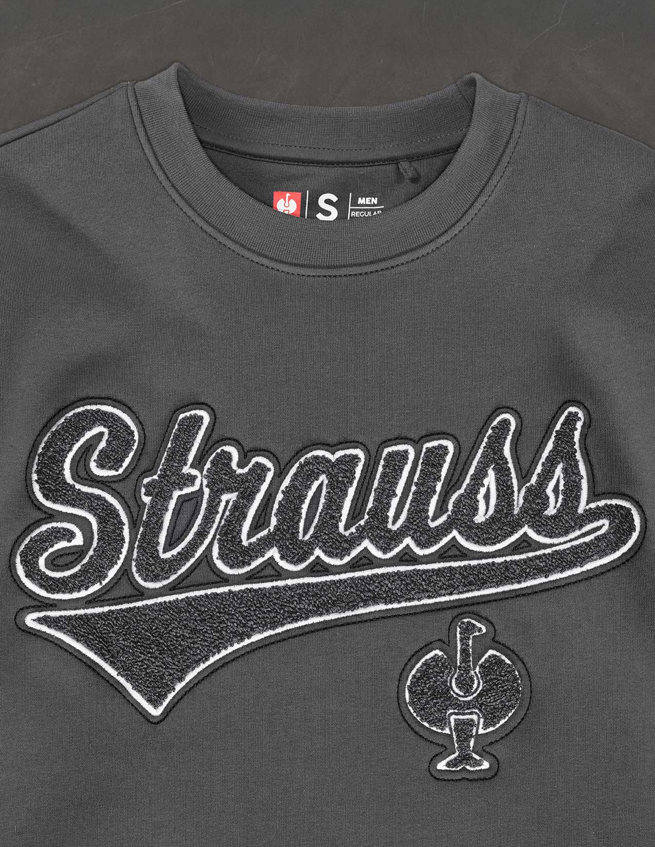 Gray sweatshirt with 'Strauss' branding on a dark background