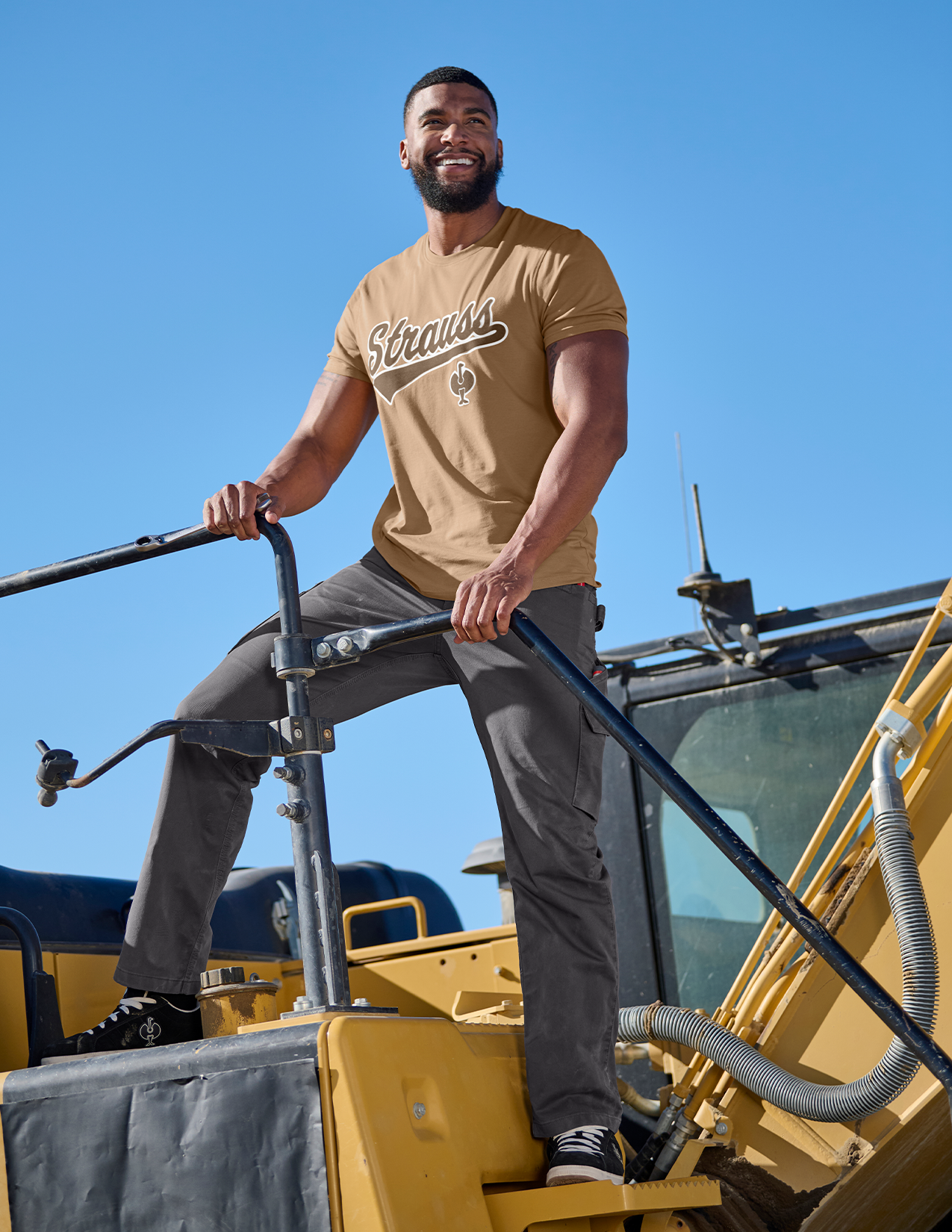 Man standing on a piece of construction equipment with a clear blue sky in the background