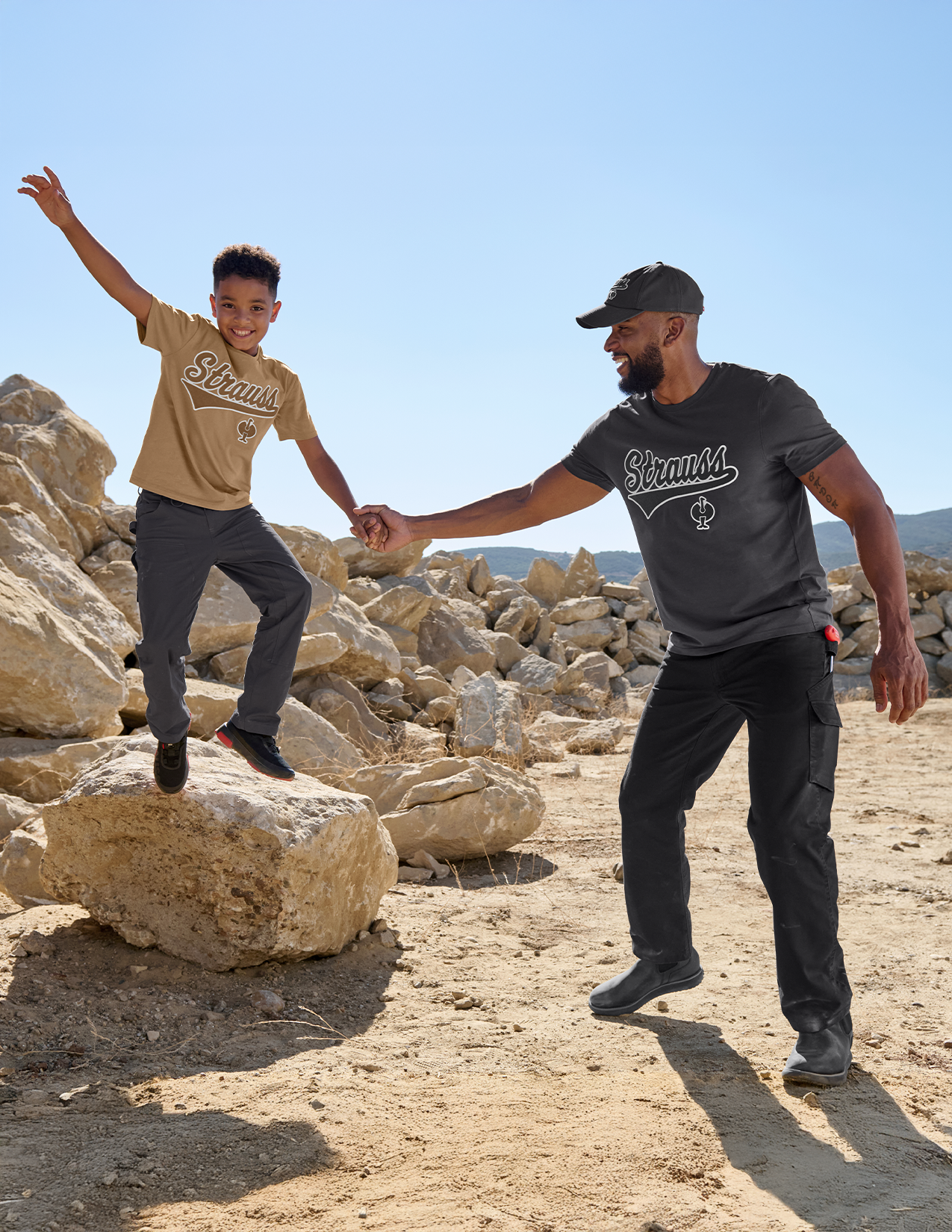 Man and child holding hands on rocky terrain with clear blue sky
