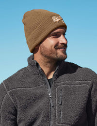 Man wearing a brown knit beanie and dark gray fleece jacket against a clear blue sky.