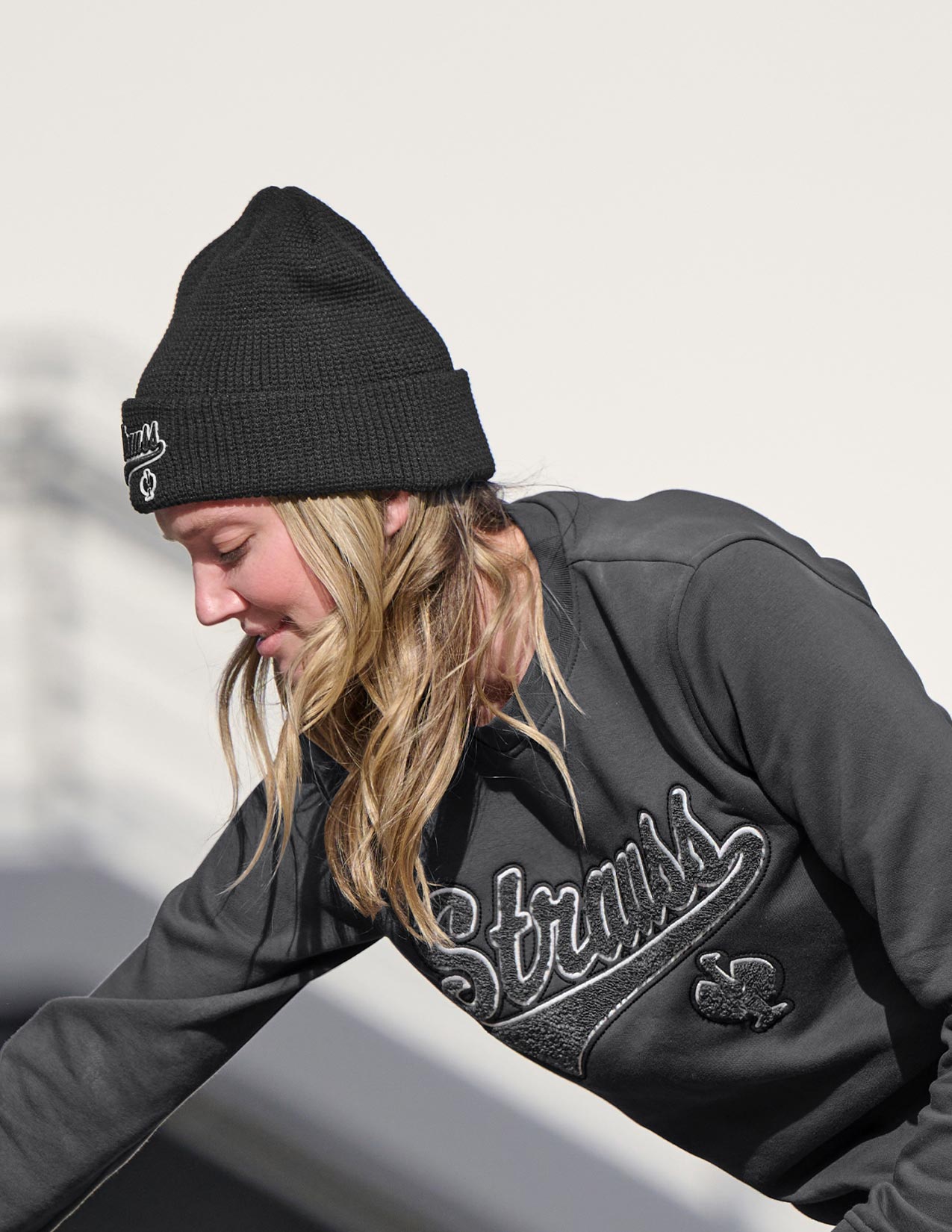 Woman wearing a black beanie and gray sweatshirt with 'Strauss' branding.