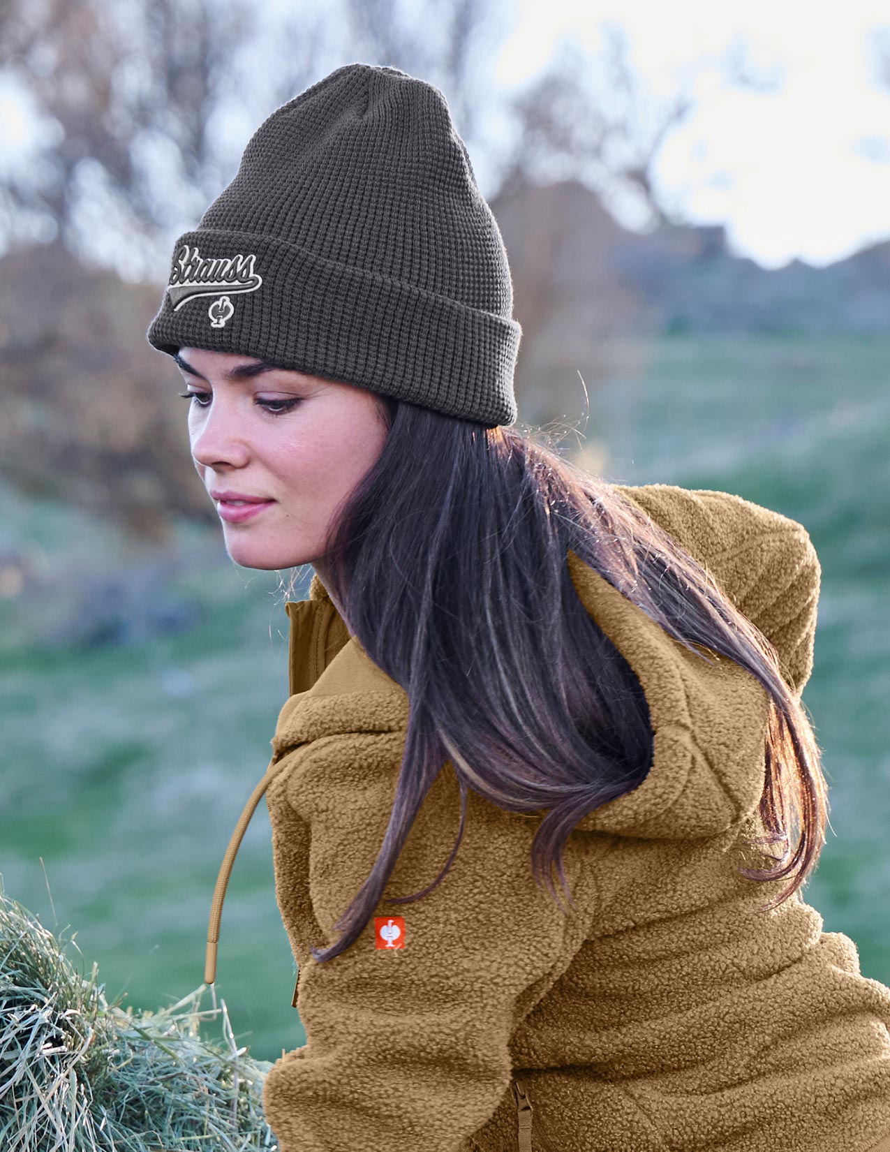 Woman wearing a dark grey beanie and brown jacket outdoors
