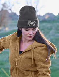 Woman wearing a brown jacket and grey beanie with 'Strauss' logo outdoors.