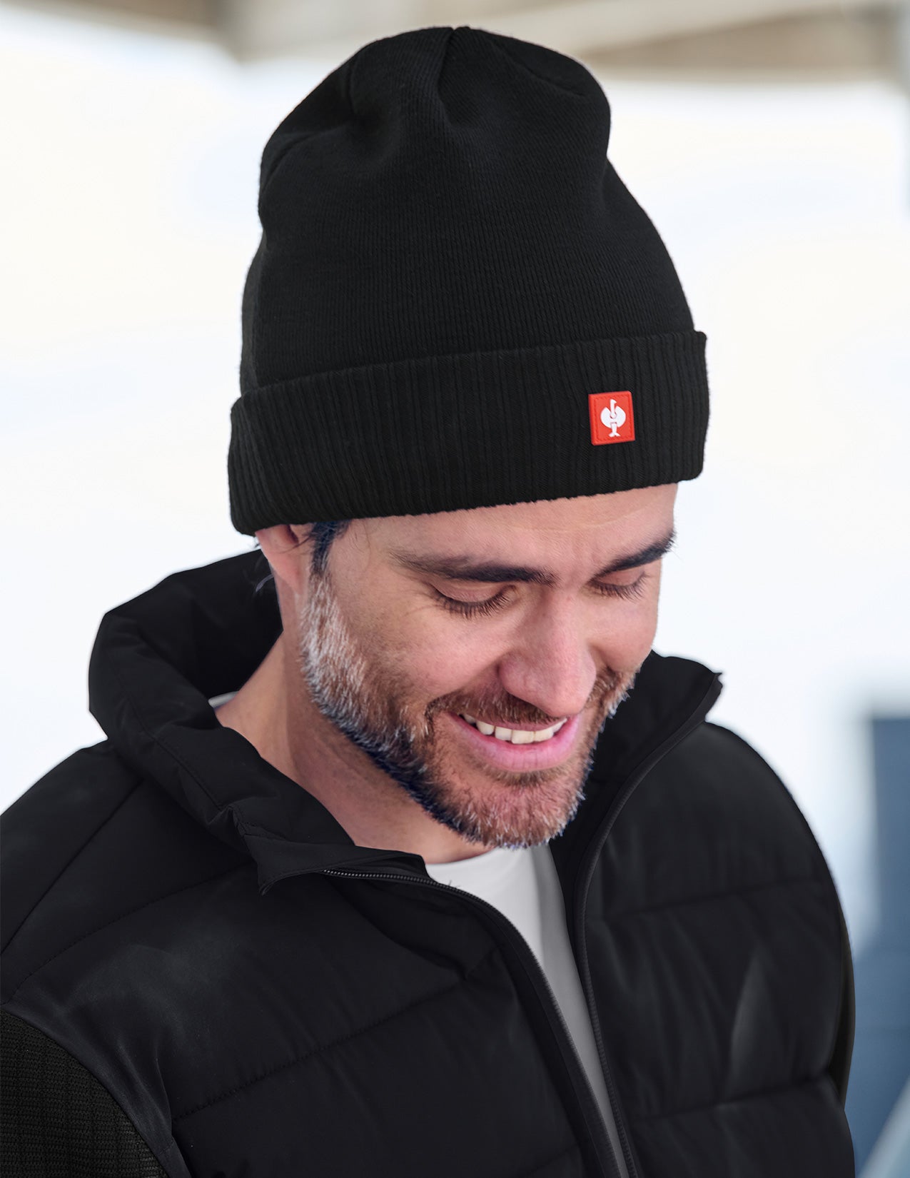 Man wearing a black beanie with a red logo, looking down.