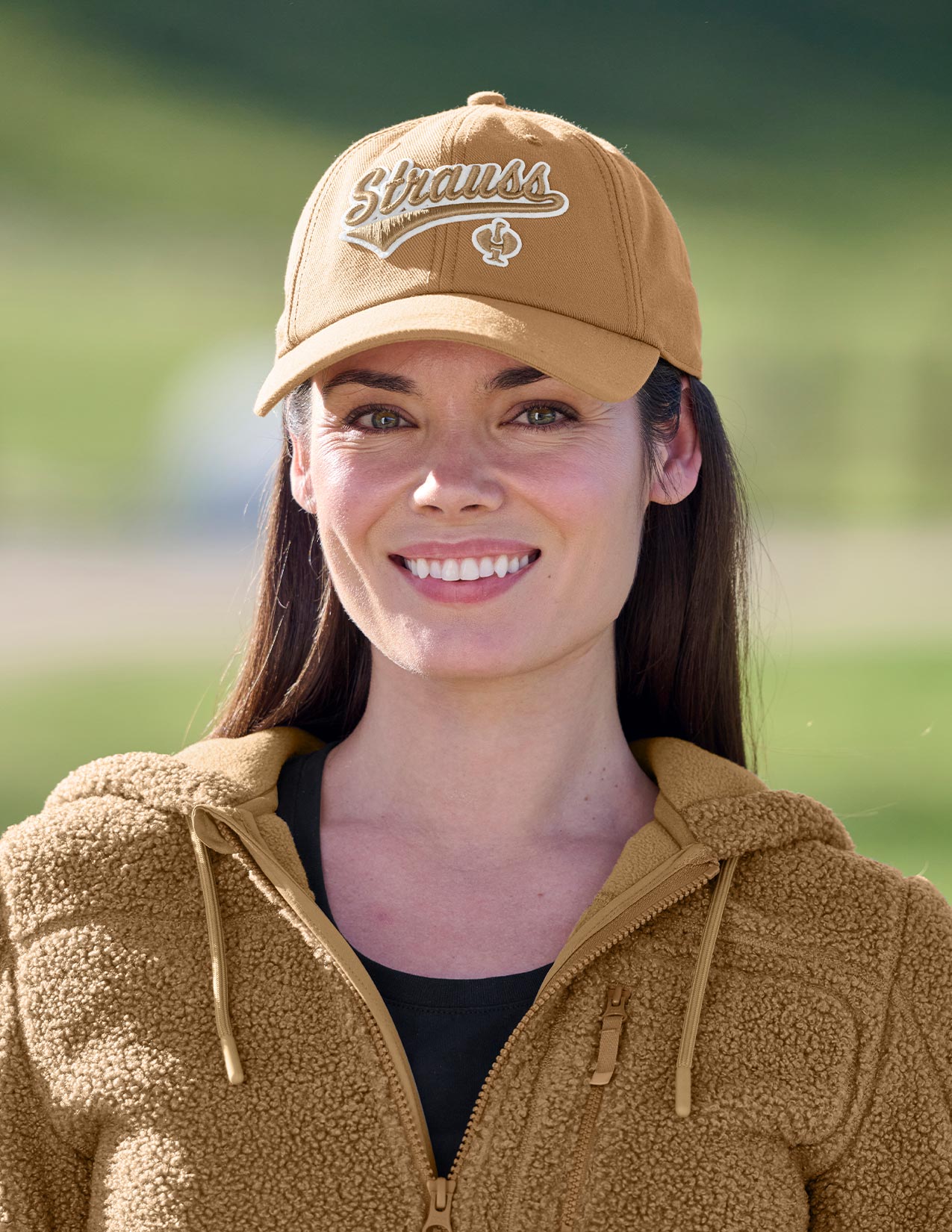 Woman wearing a tan cap and jacket with 'Strauss' logo outdoors