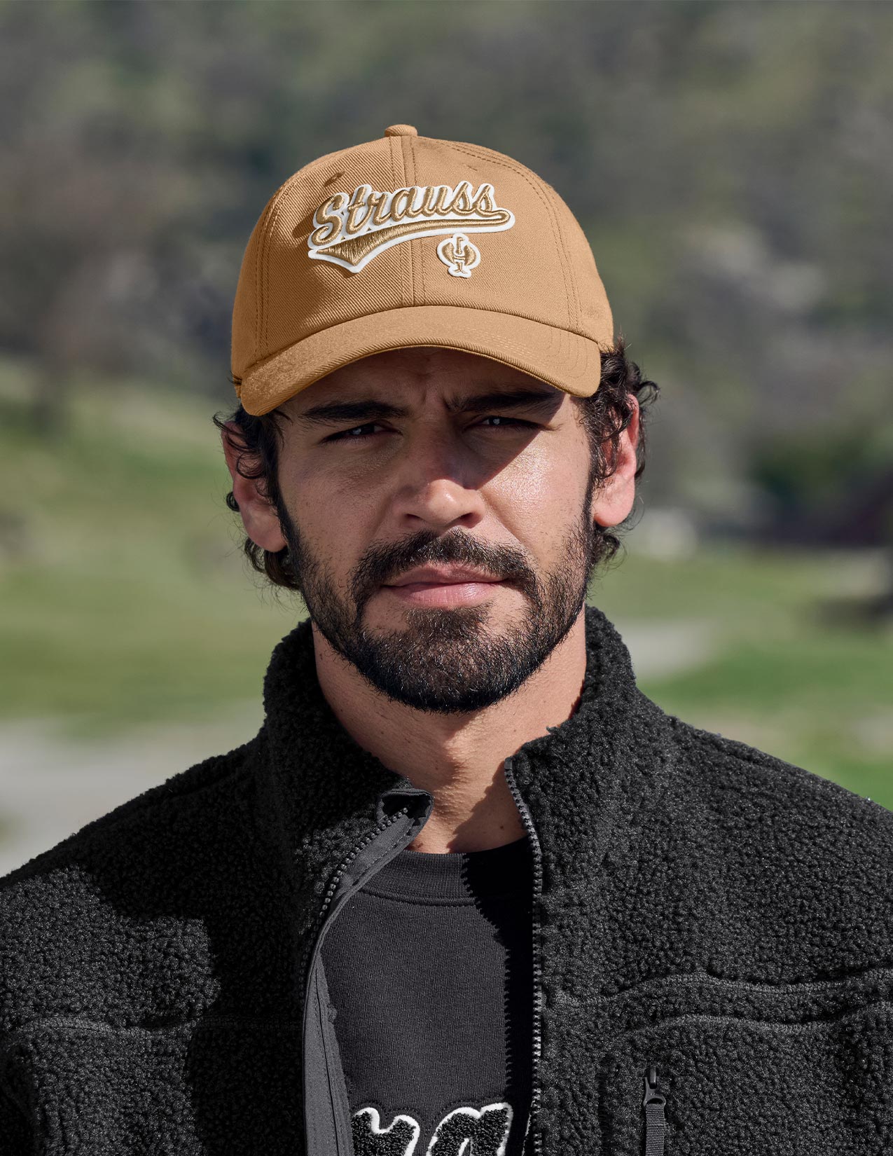 Man wearing a brown cap with 'Strauss' logo and black jacket outdoors