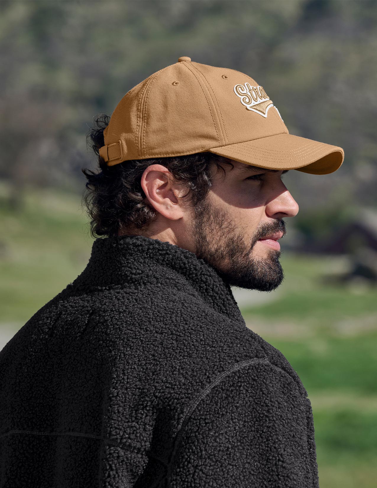 Man wearing a brown cap with a logo, standing outdoors.