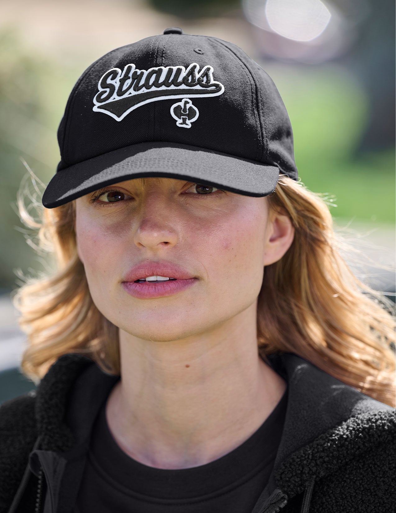 Woman wearing a black cap with 'Strauss' branding outdoors