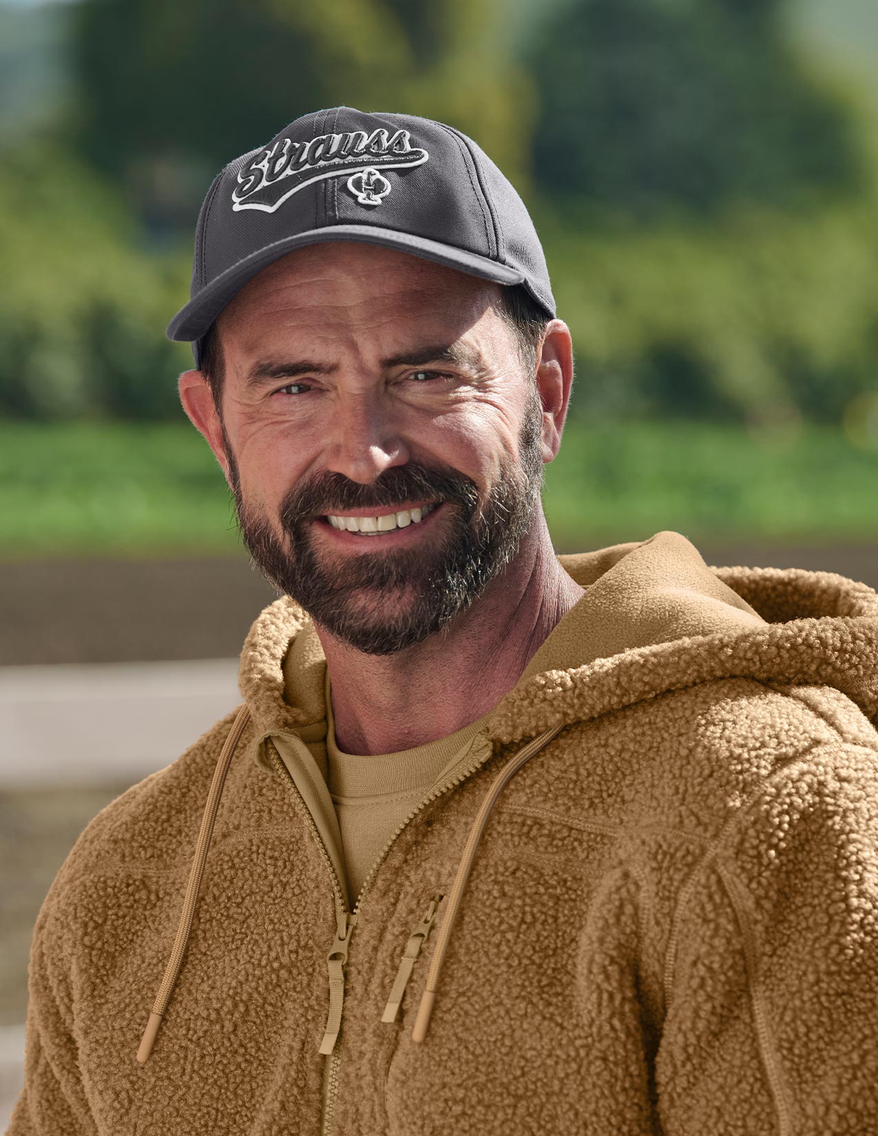 Man wearing a cap and brown jacket with a blurred green background