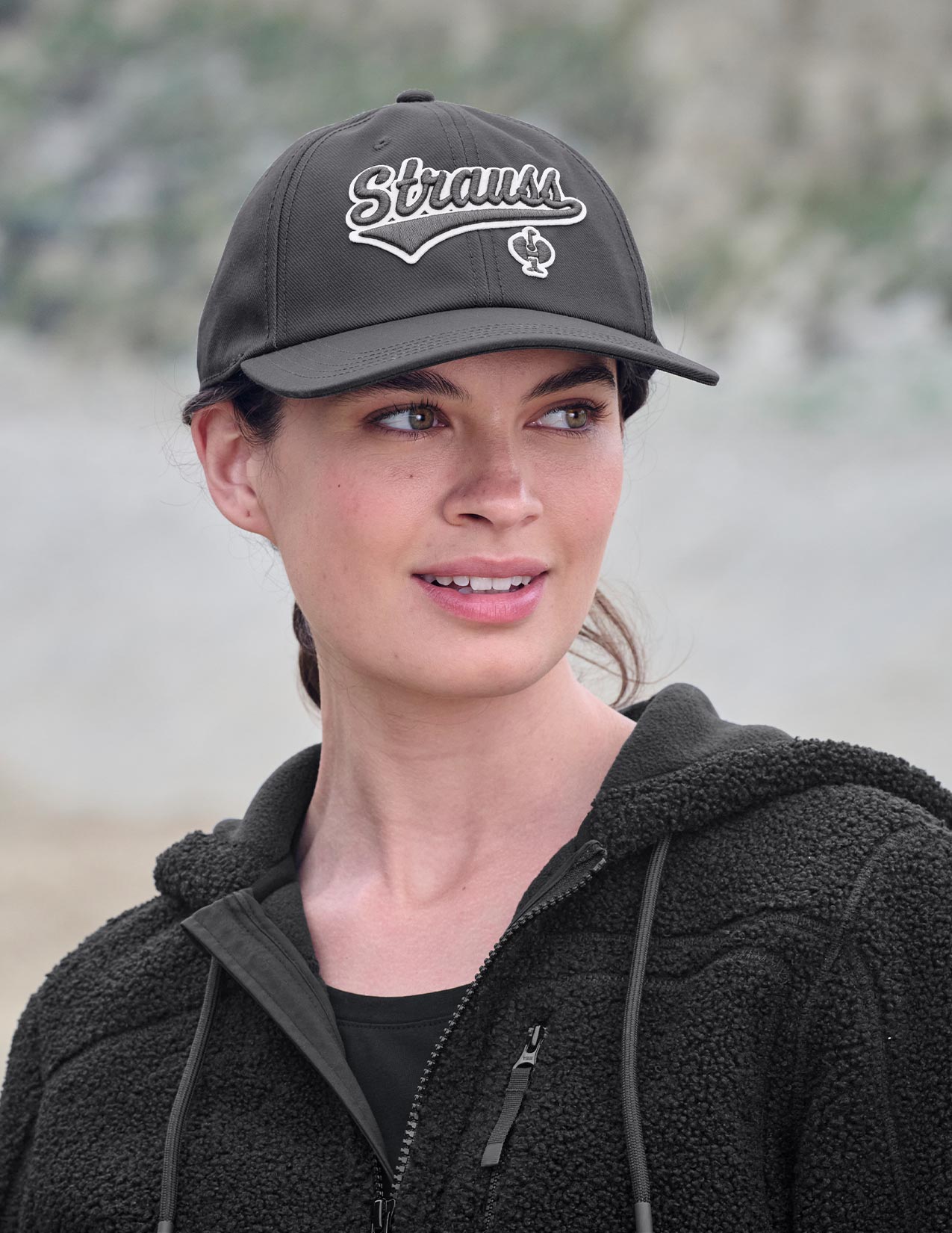 Woman wearing a black cap with 'Strauss' branding outdoors