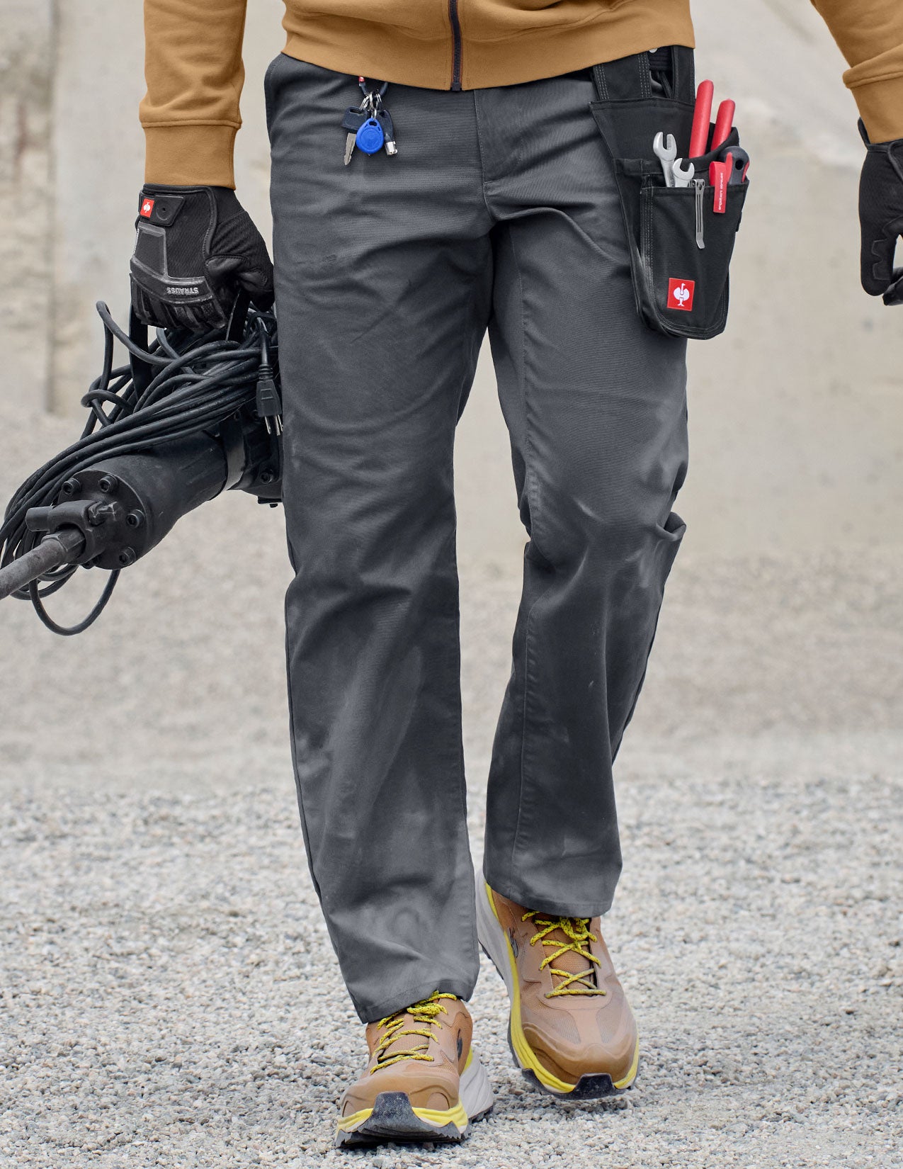 Person wearing gray work pants with tool belt and gloves, standing on a concrete surface.