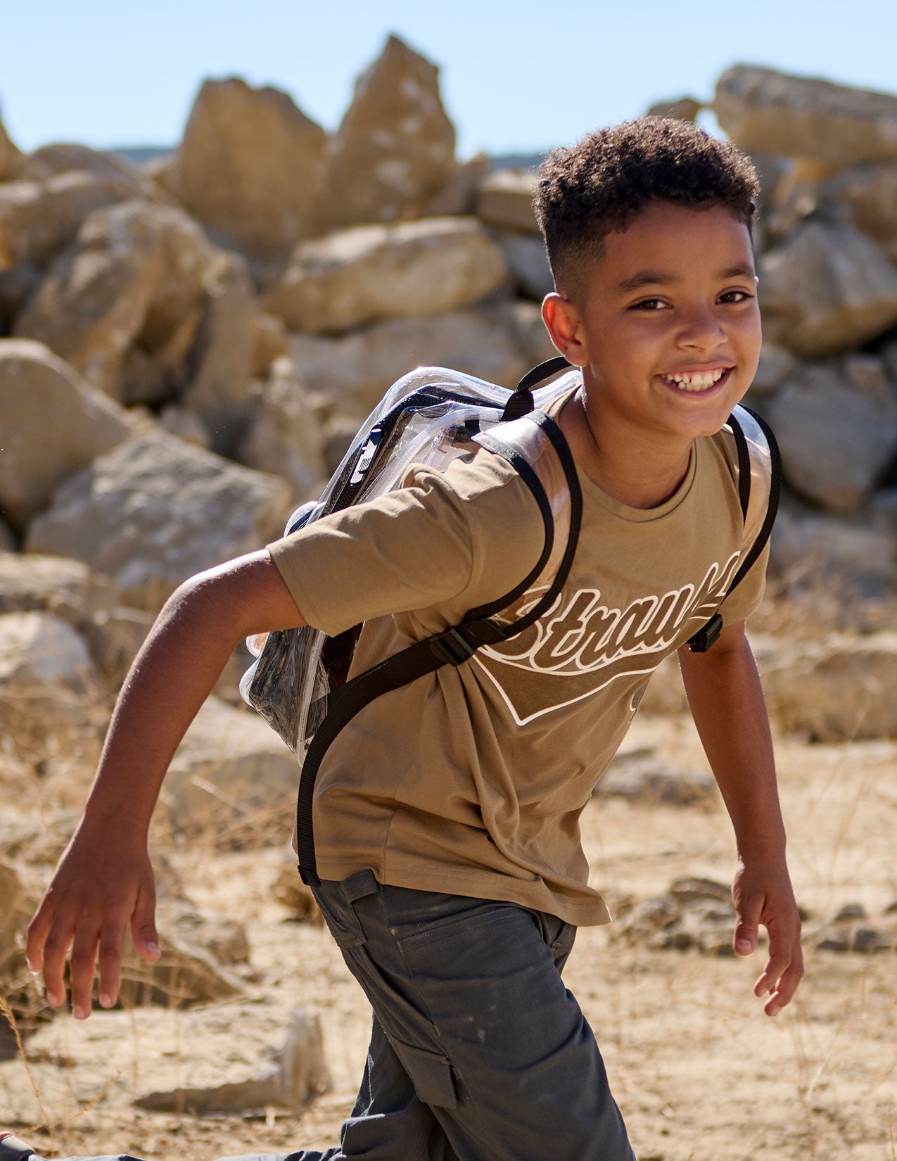 Child with a clear backpack standing in a rocky desert landscape.