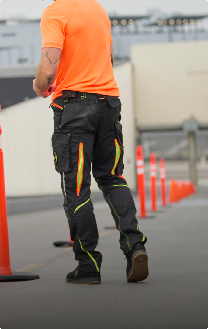 The Cargo Work Pants e.s.motion 2020 from the back with the zipper vent being cleary visible. The man is also wearing a orange high-vis T-Shirt from STRAUSS and black work shoes.