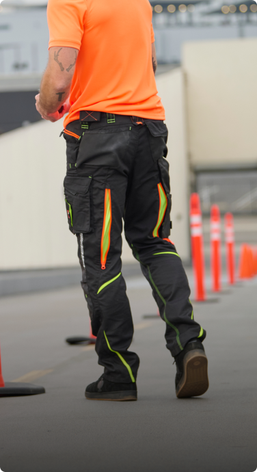 The Cargo Work Pants e.s.motion 2020 from the back with the zipper vent being cleary visible. The man is also wearing a orange high-vis T-Shirt from STRAUSS and black work shoes.