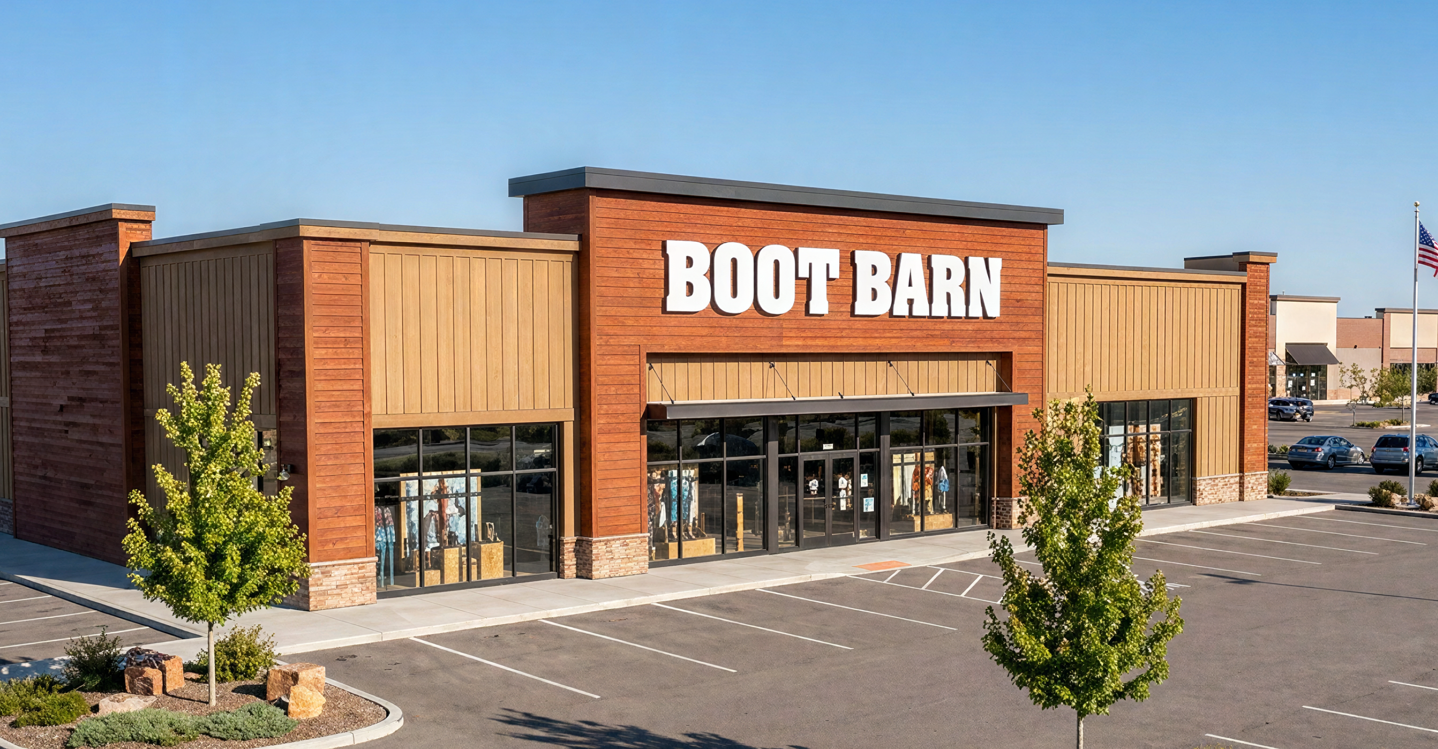 An image of a Boot Barn store. In front of the store there is a parking lot with trees.