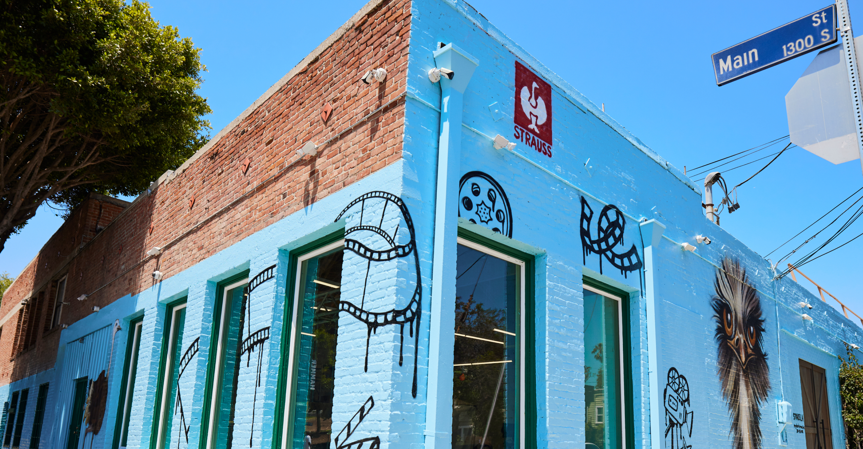 A brick building with blue paint and film reel murals stands on the corner of Main Street under a clear blue sky.