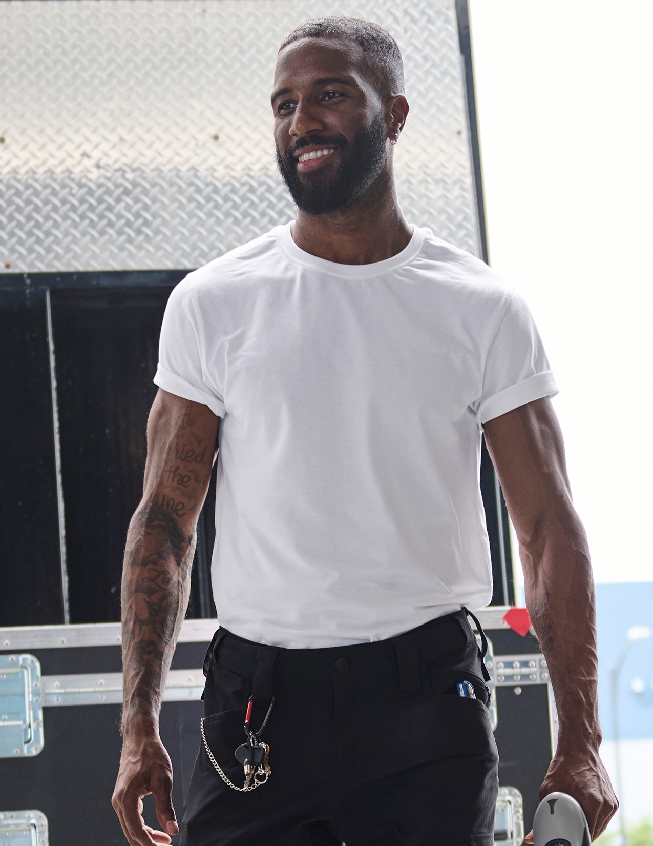 Man wearing a white t-shirt and black pants standing in front of a metallic wall.