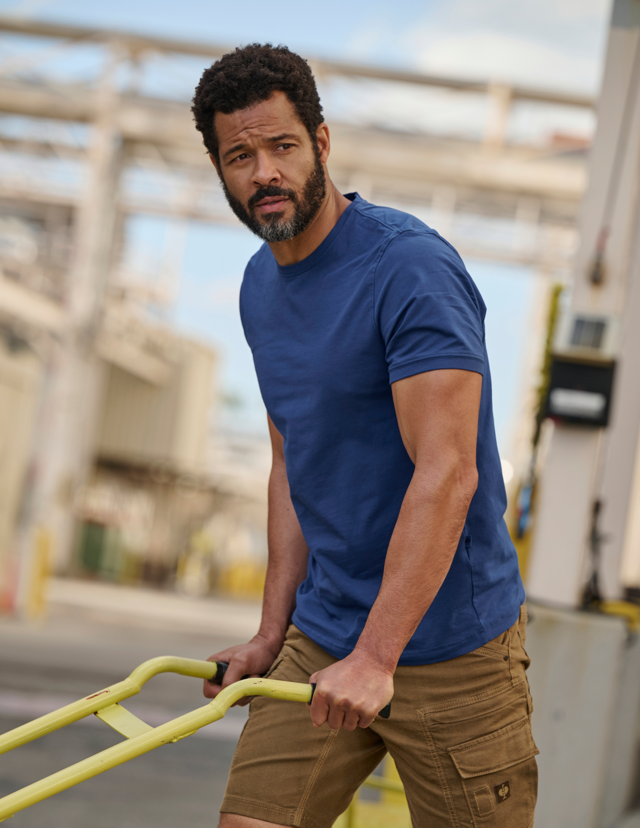 Man in a blue shirt and brown shorts standing in an industrial setting