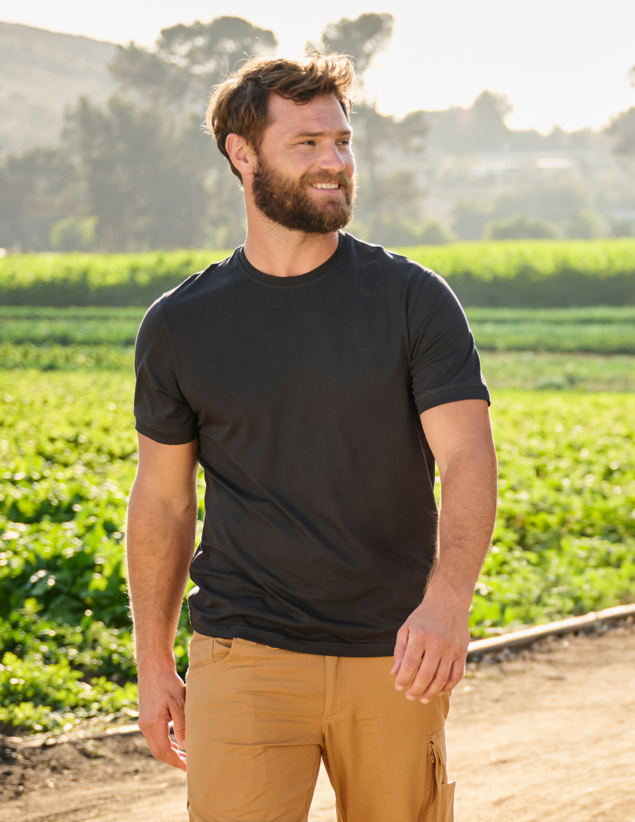Man standing in a field wearing a black t-shirt and beige pants.