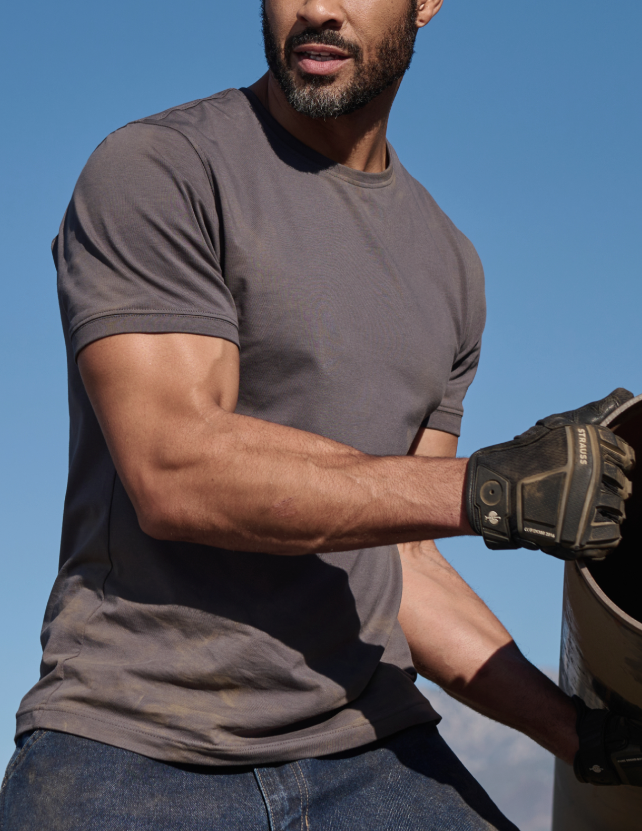 Man wearing a gray t-shirt and gloves against a blue sky