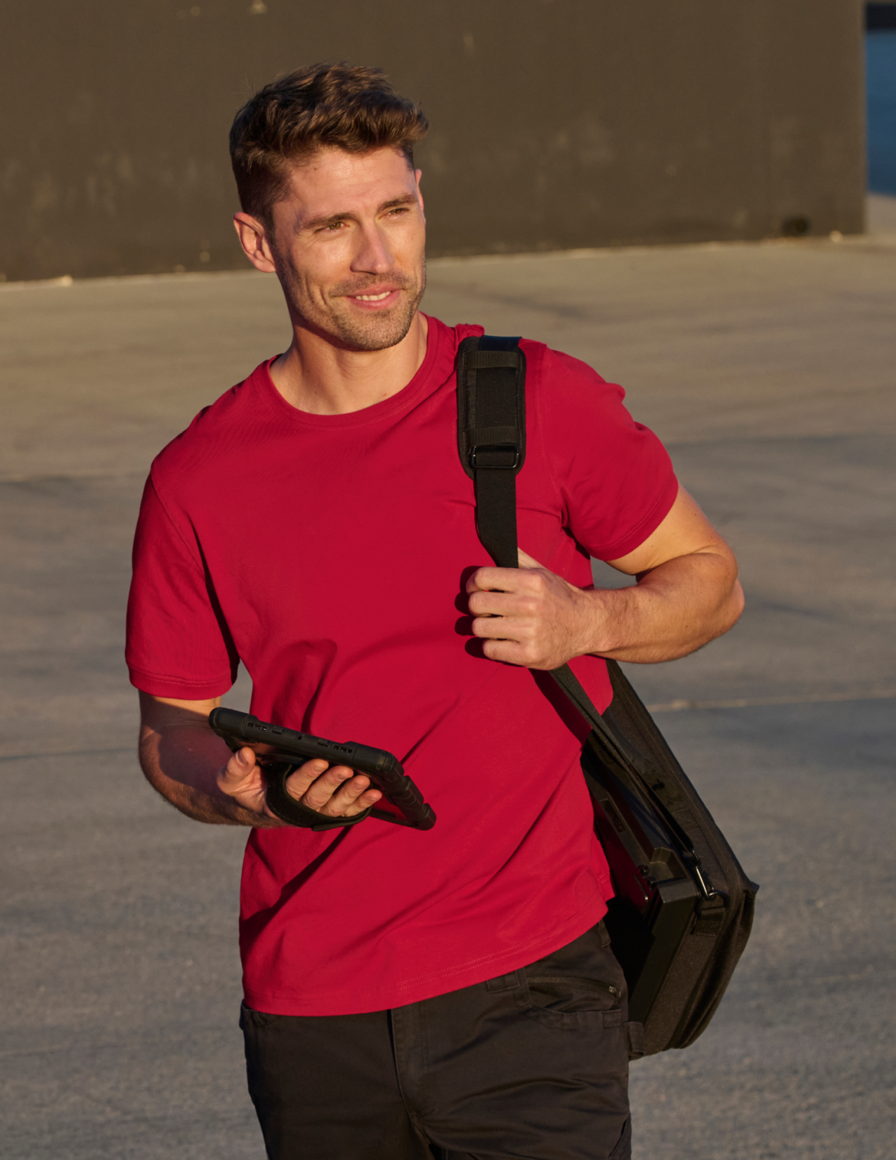 Man in a red shirt holding a black bag outdoors