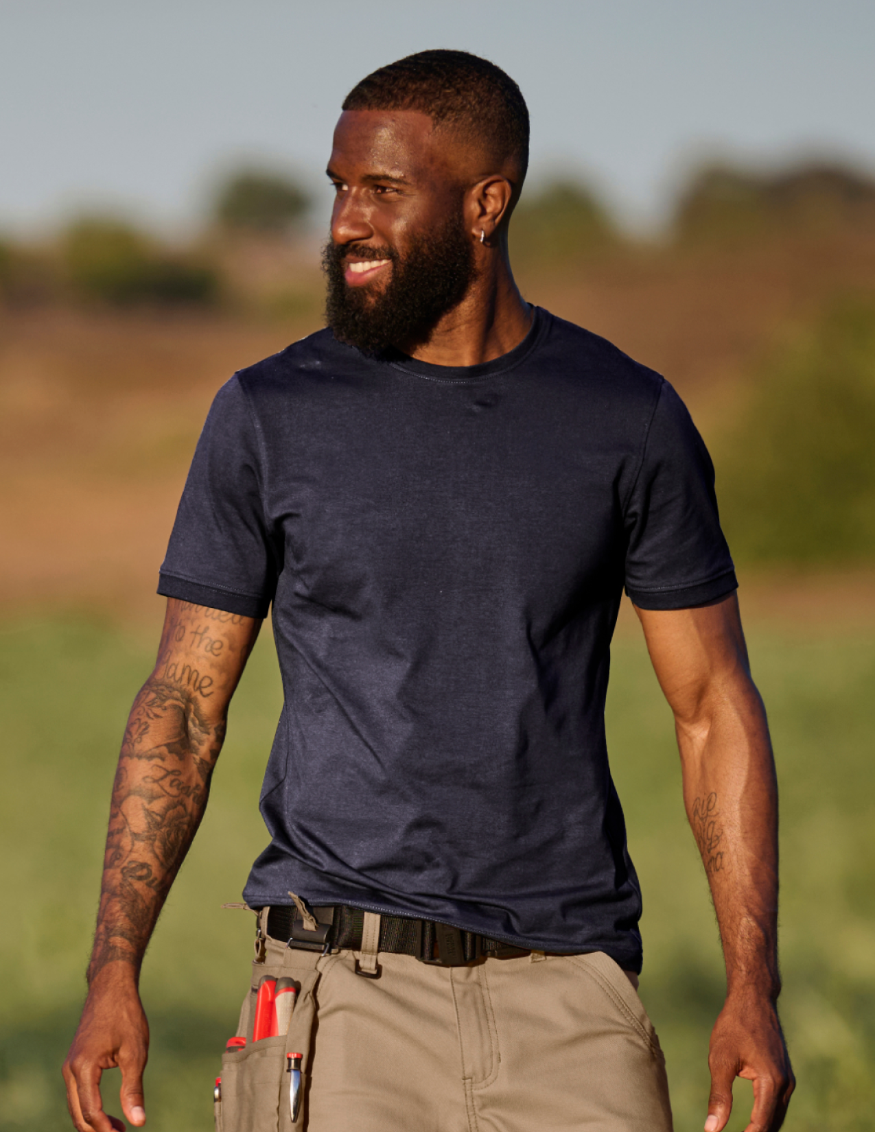 Man wearing a navy blue t-shirt and beige pants standing outdoors with a blurred natural background