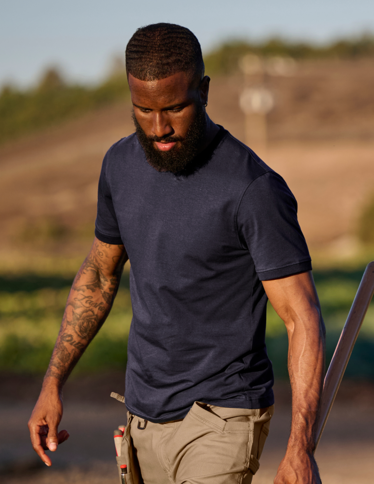 Man walking outdoors wearing a navy blue t-shirt and beige pants.