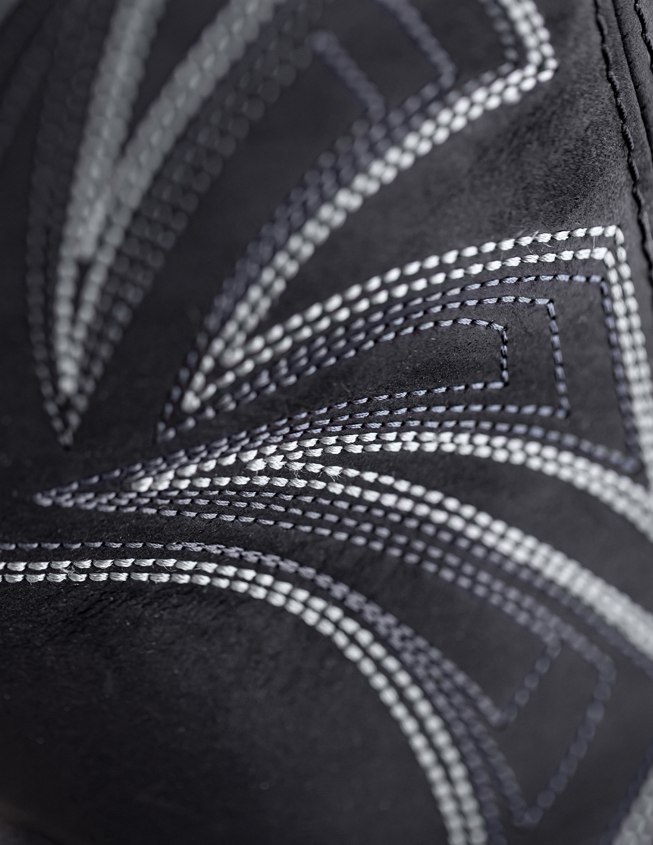 Close-up of black shoe with white stitching on a textured background