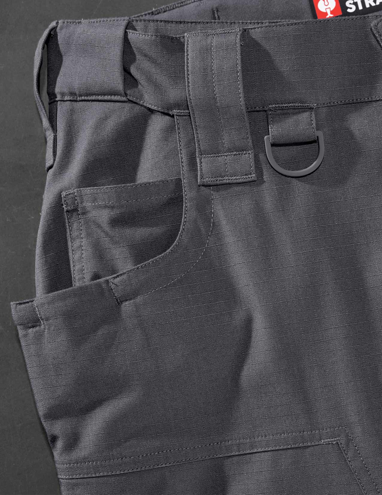 Close-up of dark gray pants with multiple pockets and a brand label on a dark background