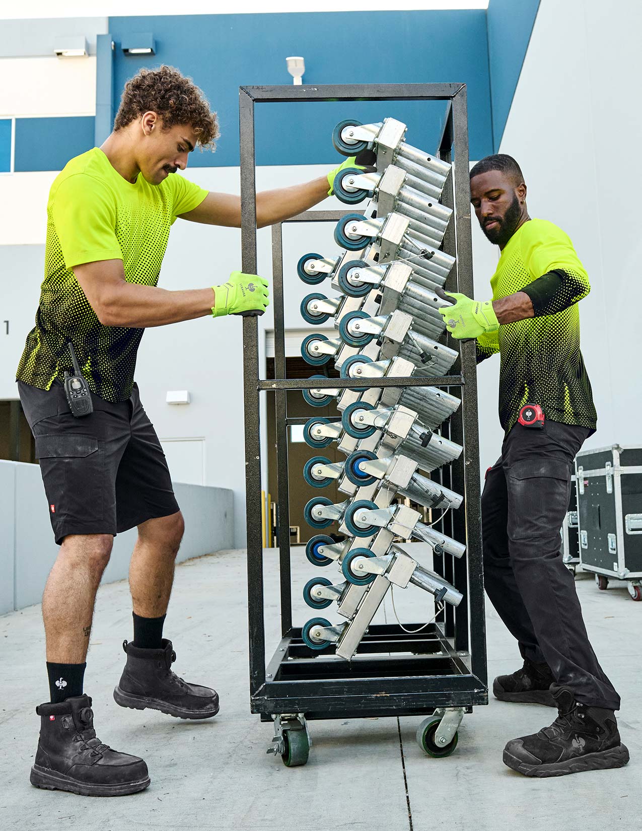 Two individuals moving a large metal rack with equipment in an indoor setting.
